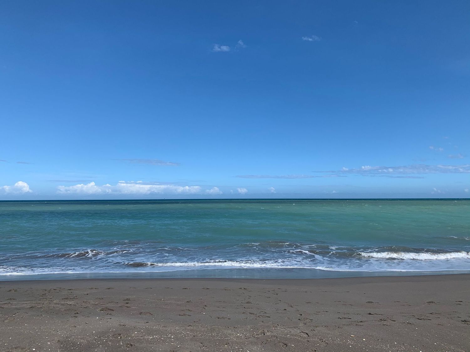 Sweeping coastal landscape with waves rolling onto an empty beach under bright blue sky.