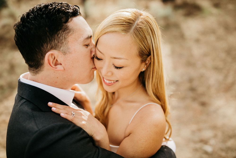 Tender moment between couple in wedding attire against natural backdrop.