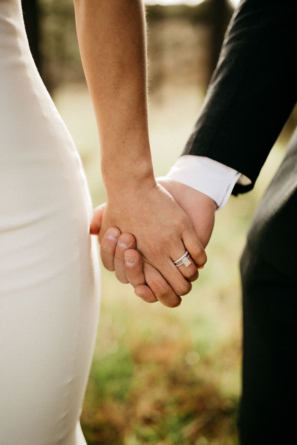 Close-up of newlywed couple holding hands, showing wedding rings and formal attire.