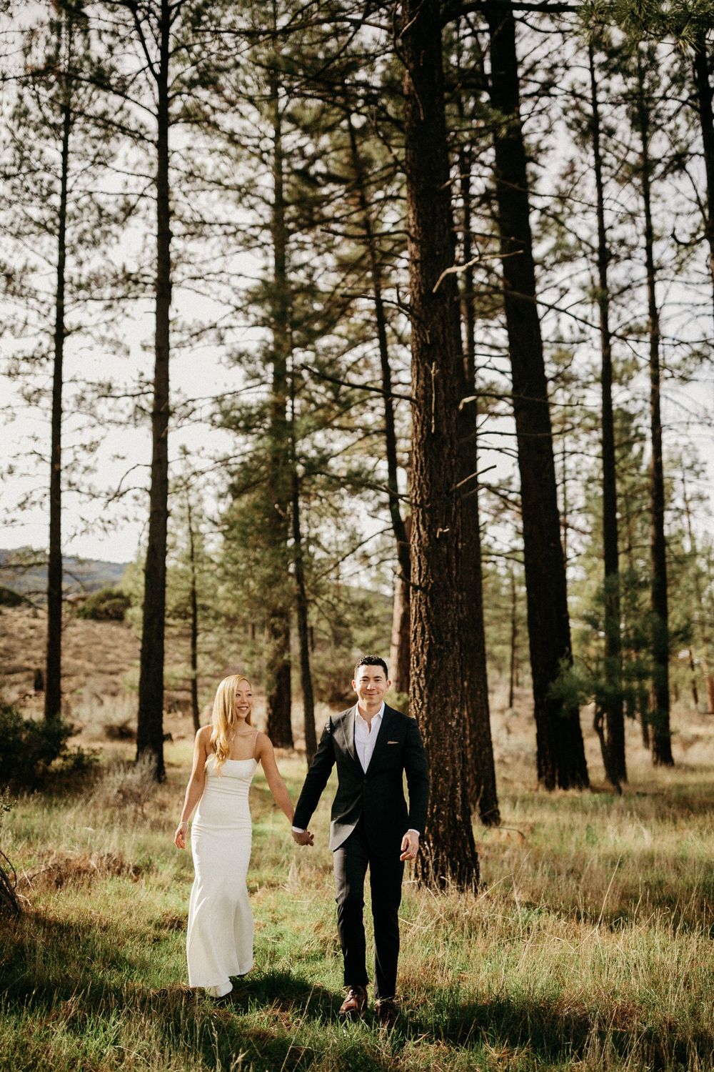 Bride and groom holding hands while walking through a serene forest setting.