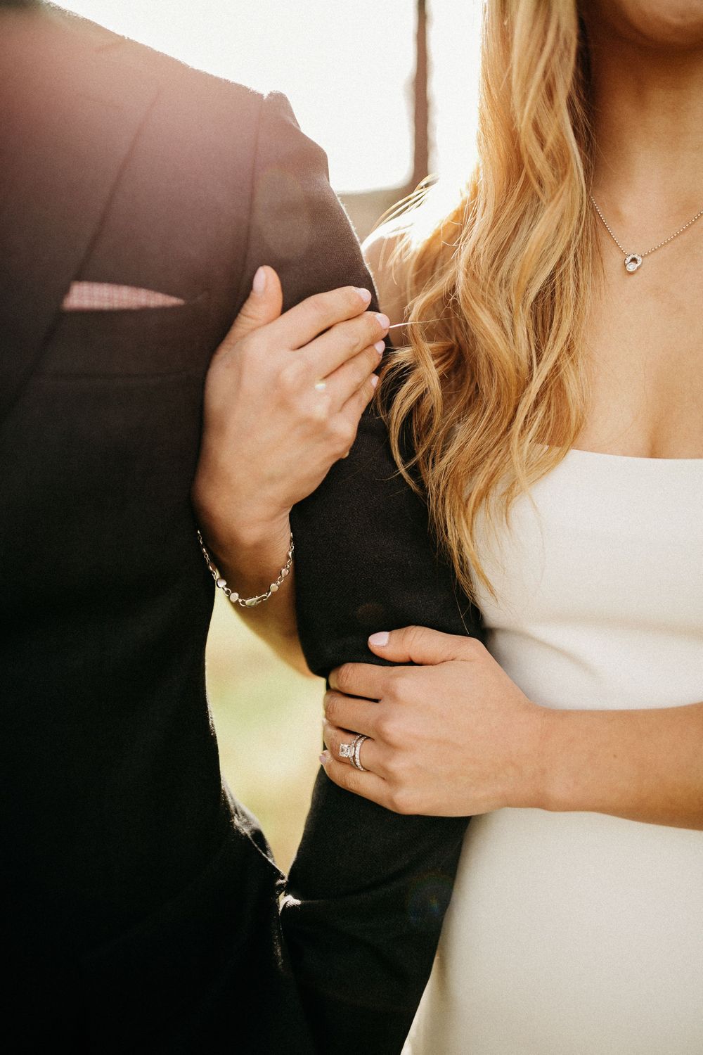 Close-up of elegant wedding attire with gold light shining through, focusing on formal black suit and white dress details.