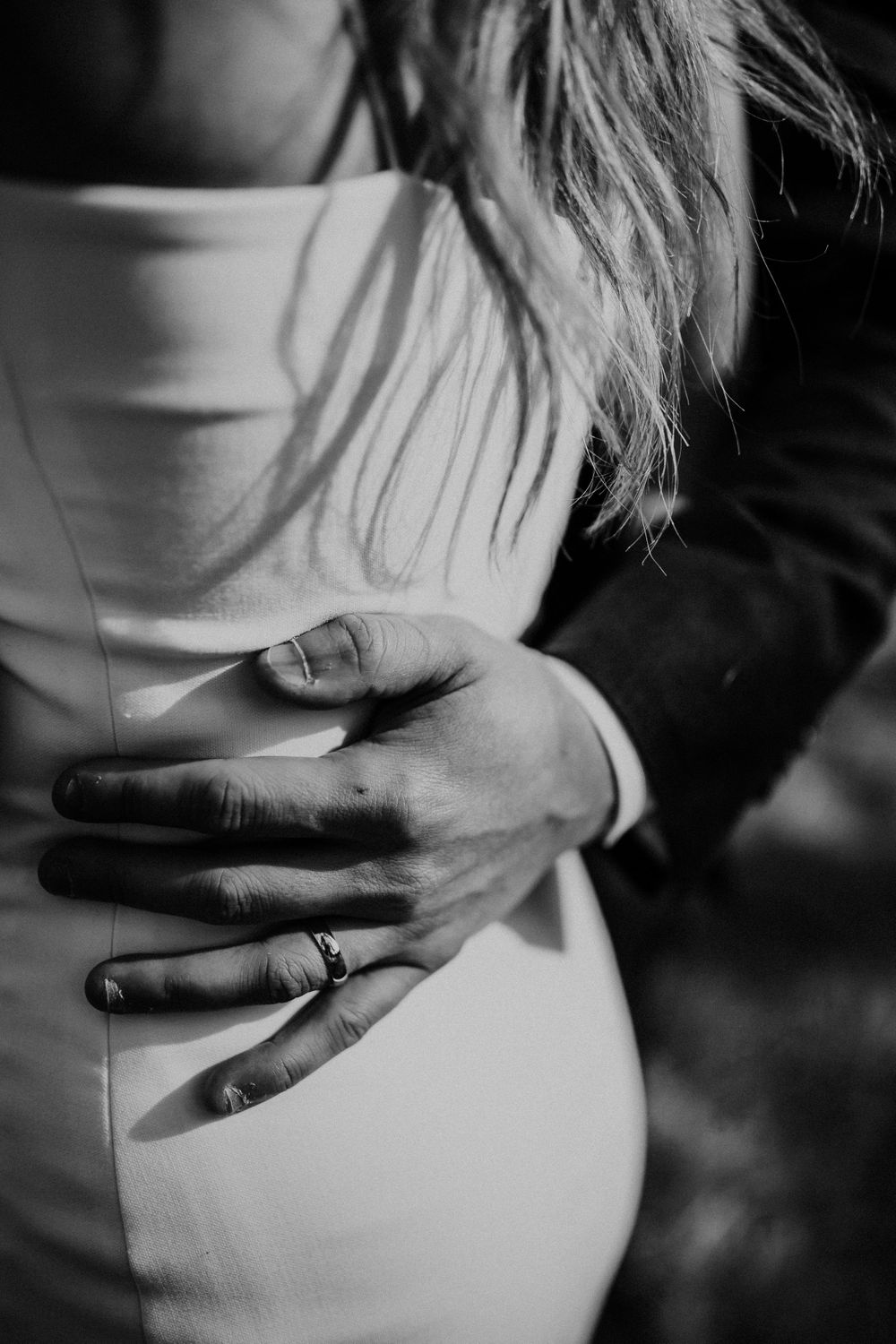 Black and white artistic shot focusing on a hand with wedding ring against white fabric.