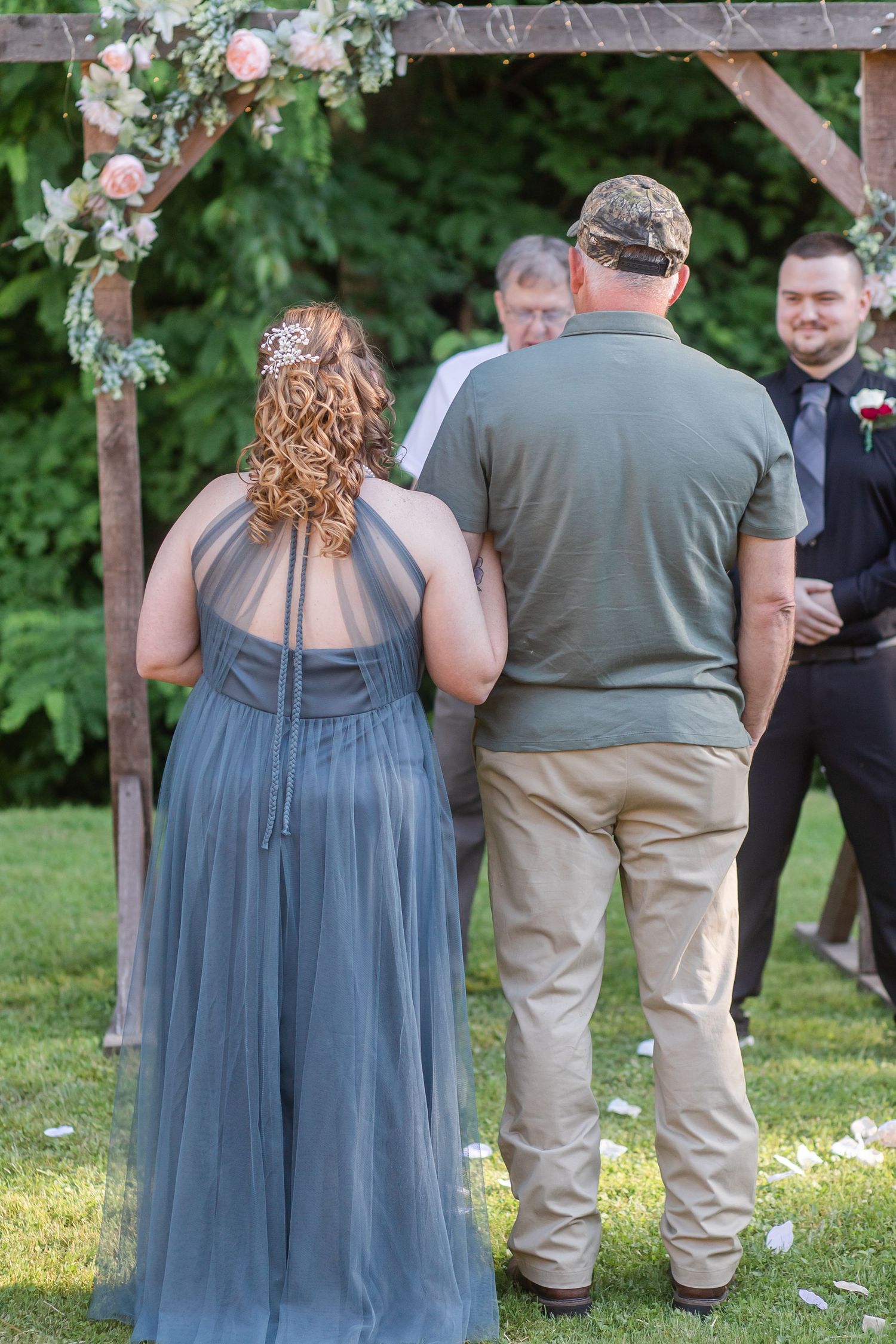Wedding guests in blue dresses and casual attire gathered under a decorated arch.