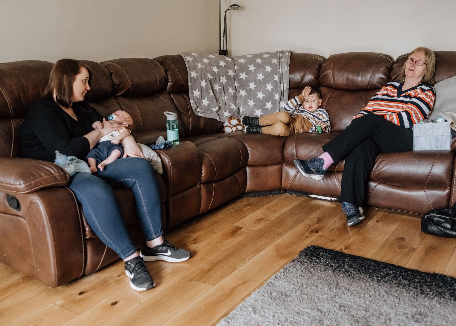 Family relaxing together on a brown leather sectional sofa in living room.