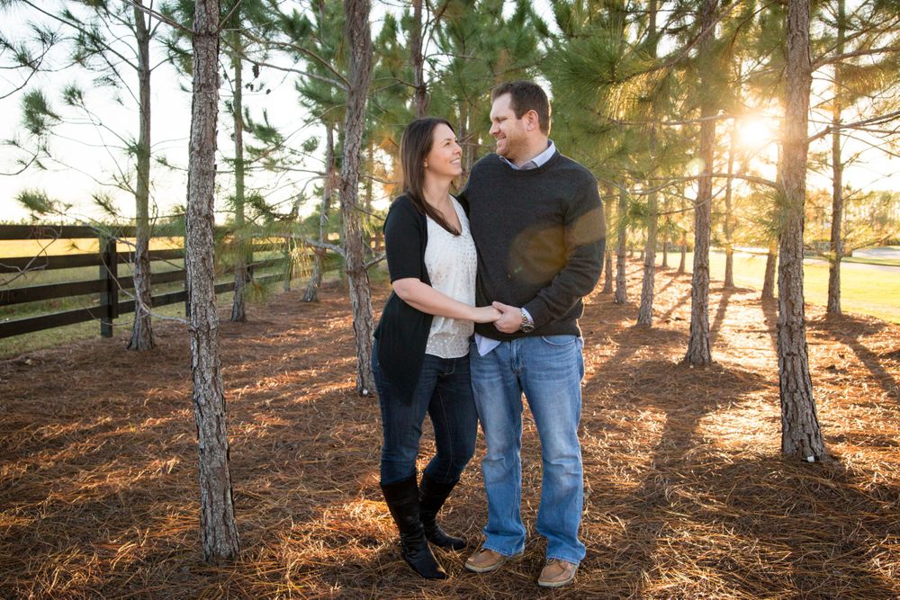 Husband and Wife holding hands looking into each others eyes while standing near the trees at sunset.