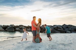 Man and woman embracing while their children run in the sand around them on the beach.