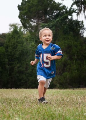Little boy running through the field wearing a football jersey.