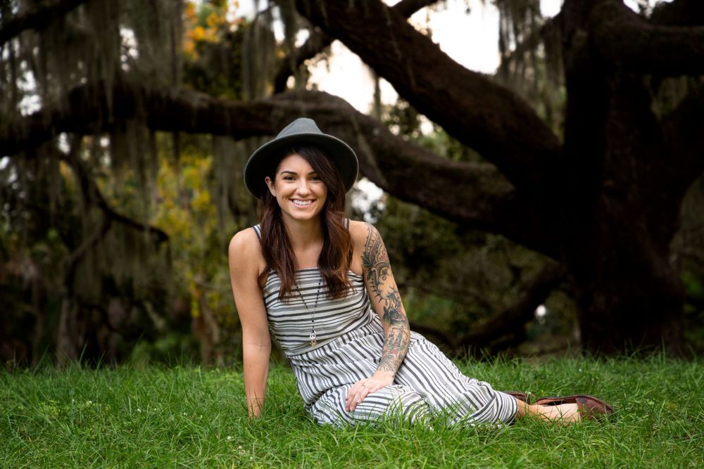 Girl in black and white dress with black hat sitting in the grass at the park.