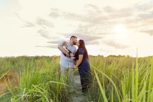 Mom and Dad kissing in a sunset field while holding their new baby.