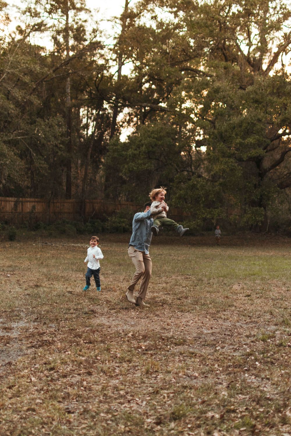 Playful family photo session in a leaf-covered field at sunset.