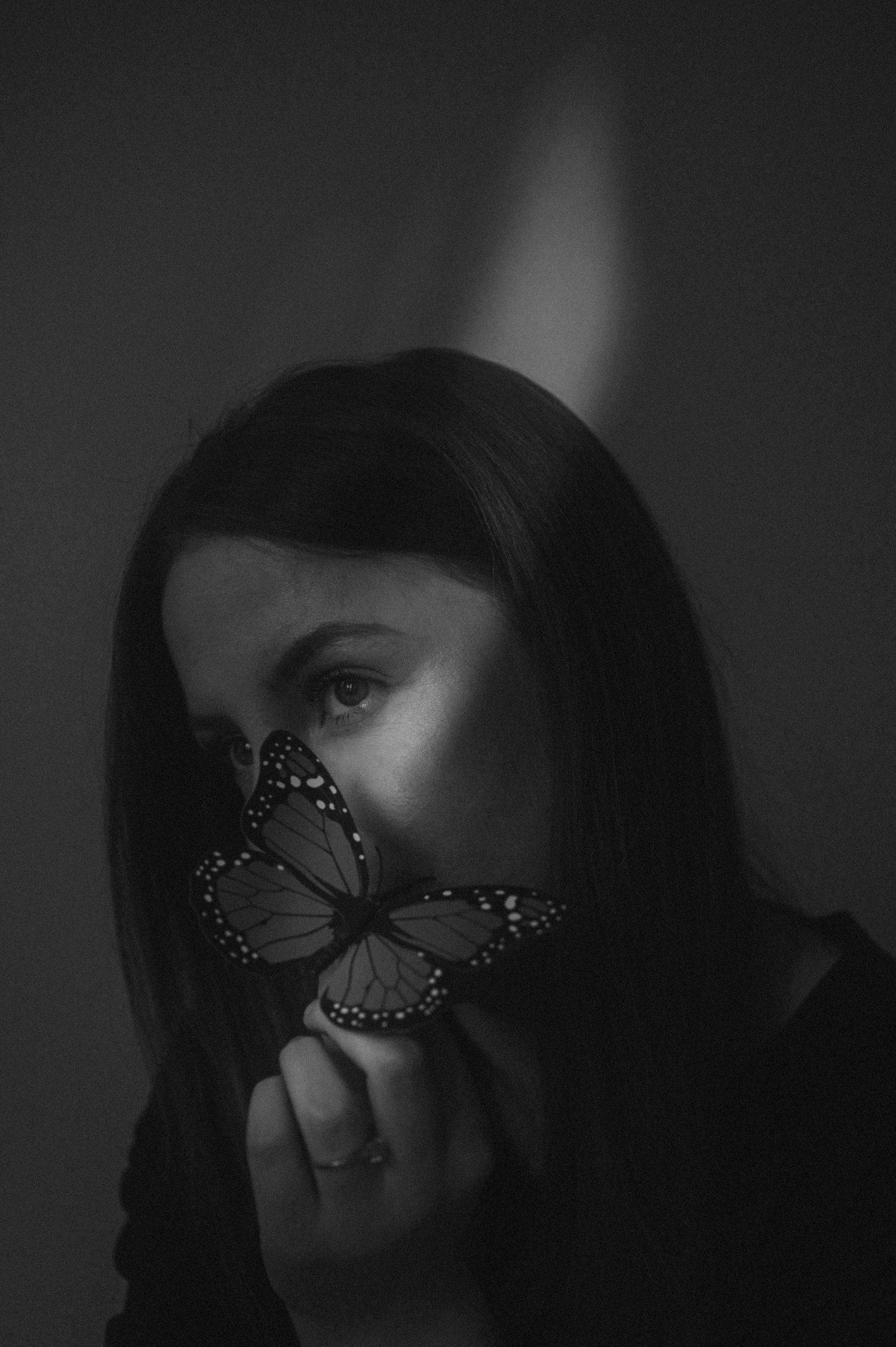 Artistic black and white portrait featuring a monarch butterfly against dark moody lighting.