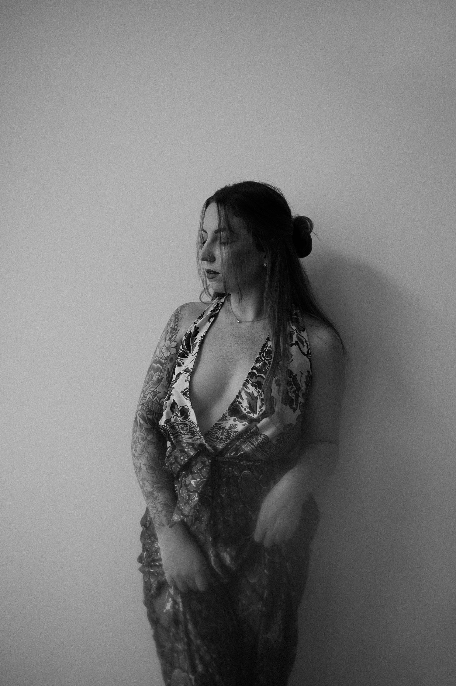 Artistic black and white portrait of a person in a lace dress against a plain wall.