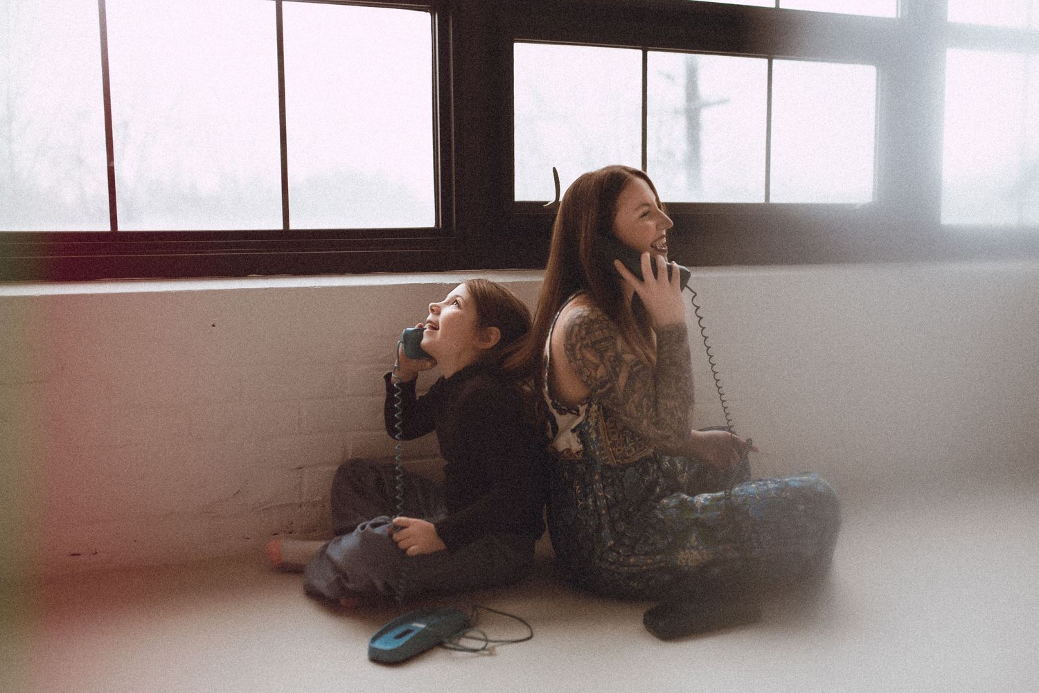 Two photographers sit back-to-back on the floor while working in an industrial space.