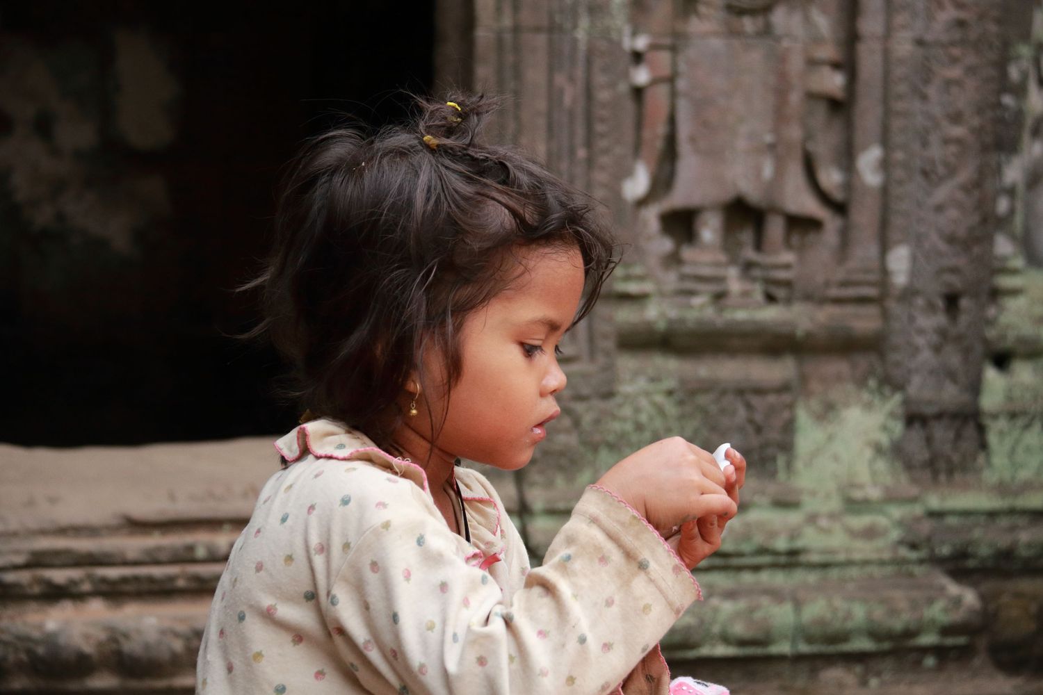 Young child examining something while sitting at ancient temple ruins.