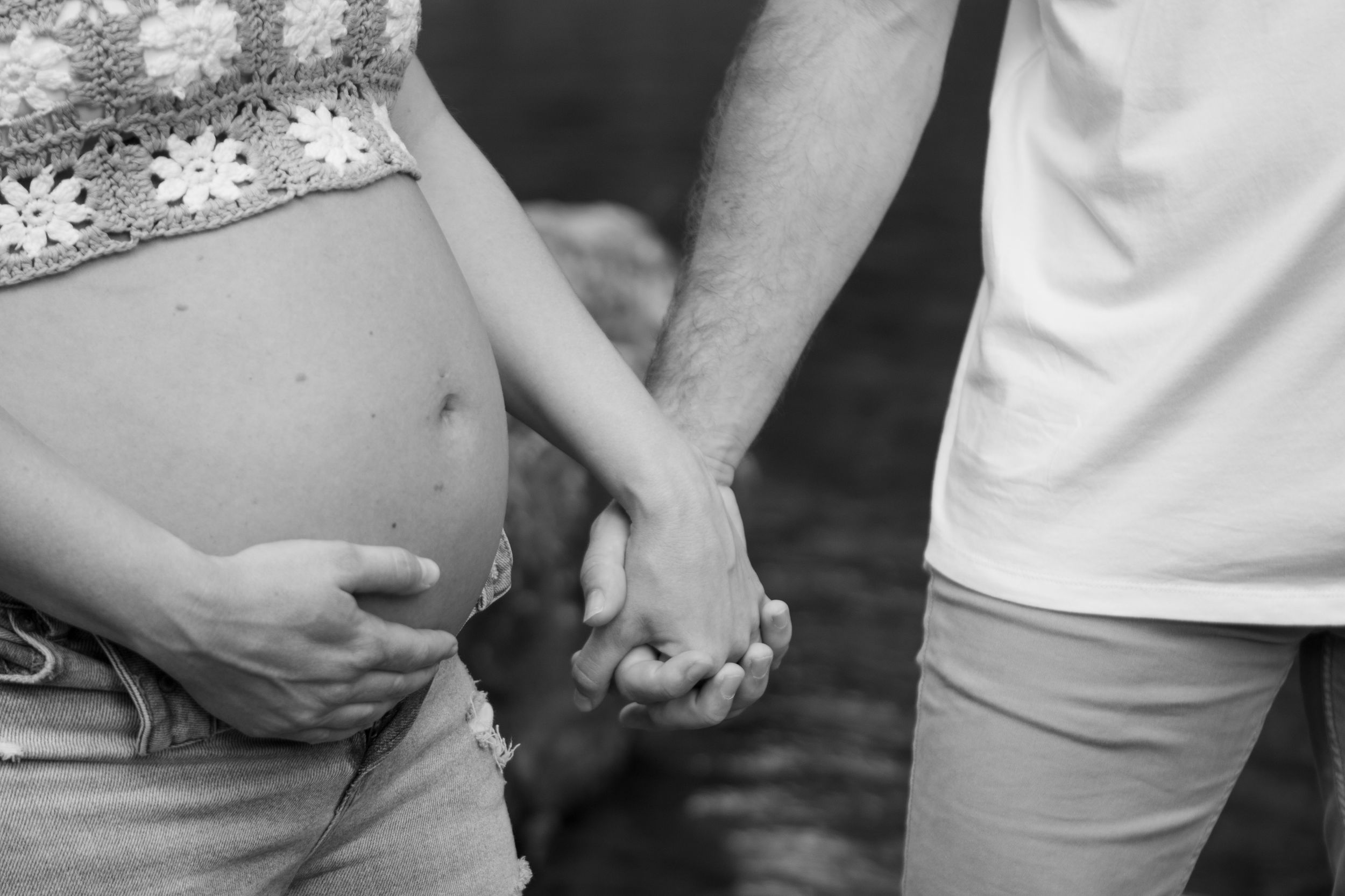Close-up black and white photo of couple holding hands during maternity shoot.
