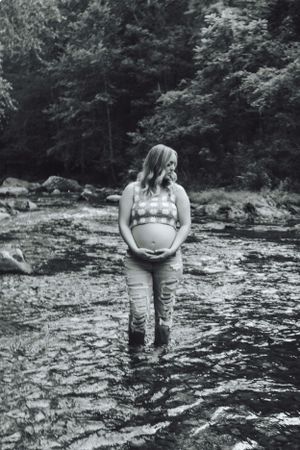 Black and white maternity portrait of an expectant mother standing in a stream.