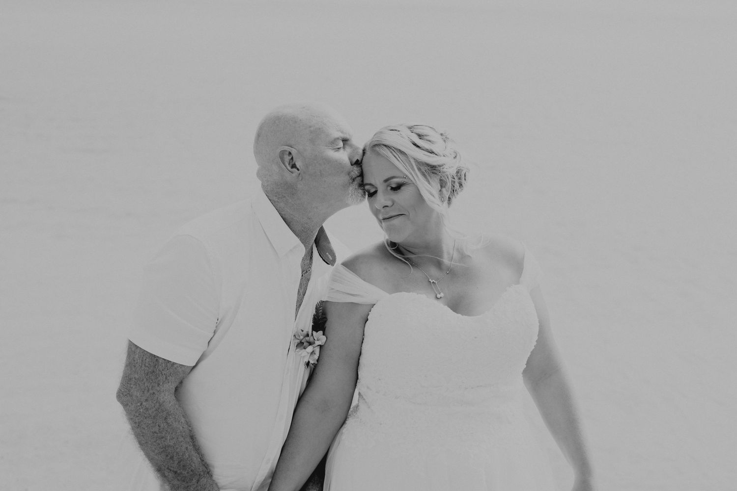 Intimate black and white portrait shows couple sharing tender moment against white background.