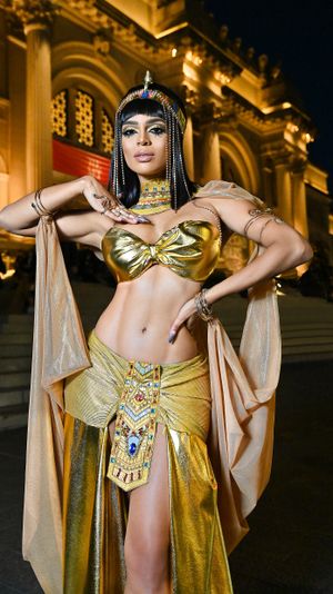 Cleopatra themed costume with ornate gold accessories against illuminated classical architecture.