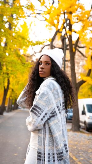 Winter fashion look with white beanie and patterned cardigan against yellow fall foliage.