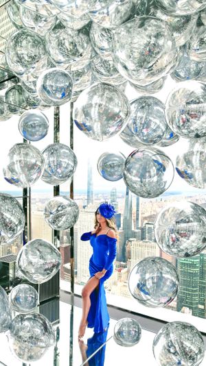 An elegant blue dress contrasts against silver disco balls with a city skyline backdrop.