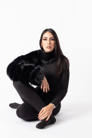 Studio fashion portrait in all black outfit with fur accessory against white background.