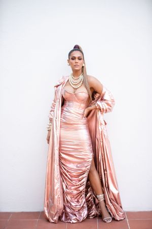 Luxurious rose gold ruched gown with matching coat and pearl necklaces on terracotta tiles.