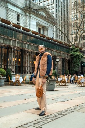 Street fashion shot featuring brown fur vest and khaki pants outside classic city architecture.