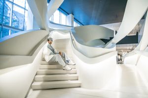 Modern white architectural interior with curved staircase and figure in casual attire.