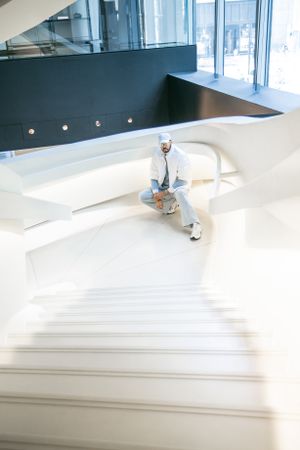 Figure in white outfit sitting on sleek modern white staircase in sunlit building.