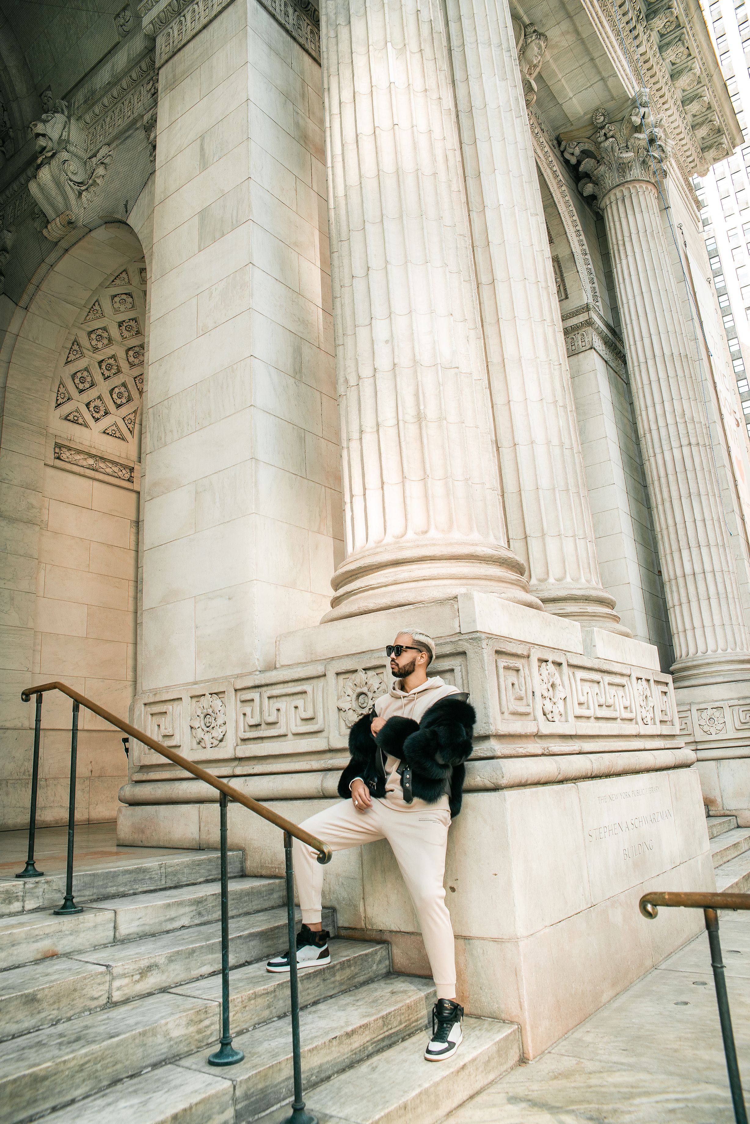 Casual figure posing on steps of classical building with ornate columns.