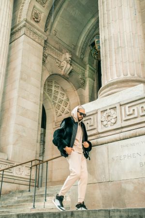Casual figure descending steps of ornate architectural building with columns.
