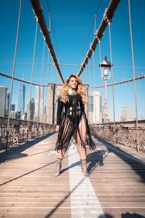 Dramatic fashion photo on Brooklyn Bridge walkway with city skyline and suspension cables.