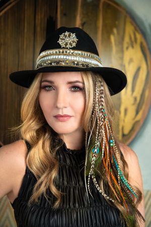 Fashionable black hat adorned with ornate jeweled band and colorful feather accents.