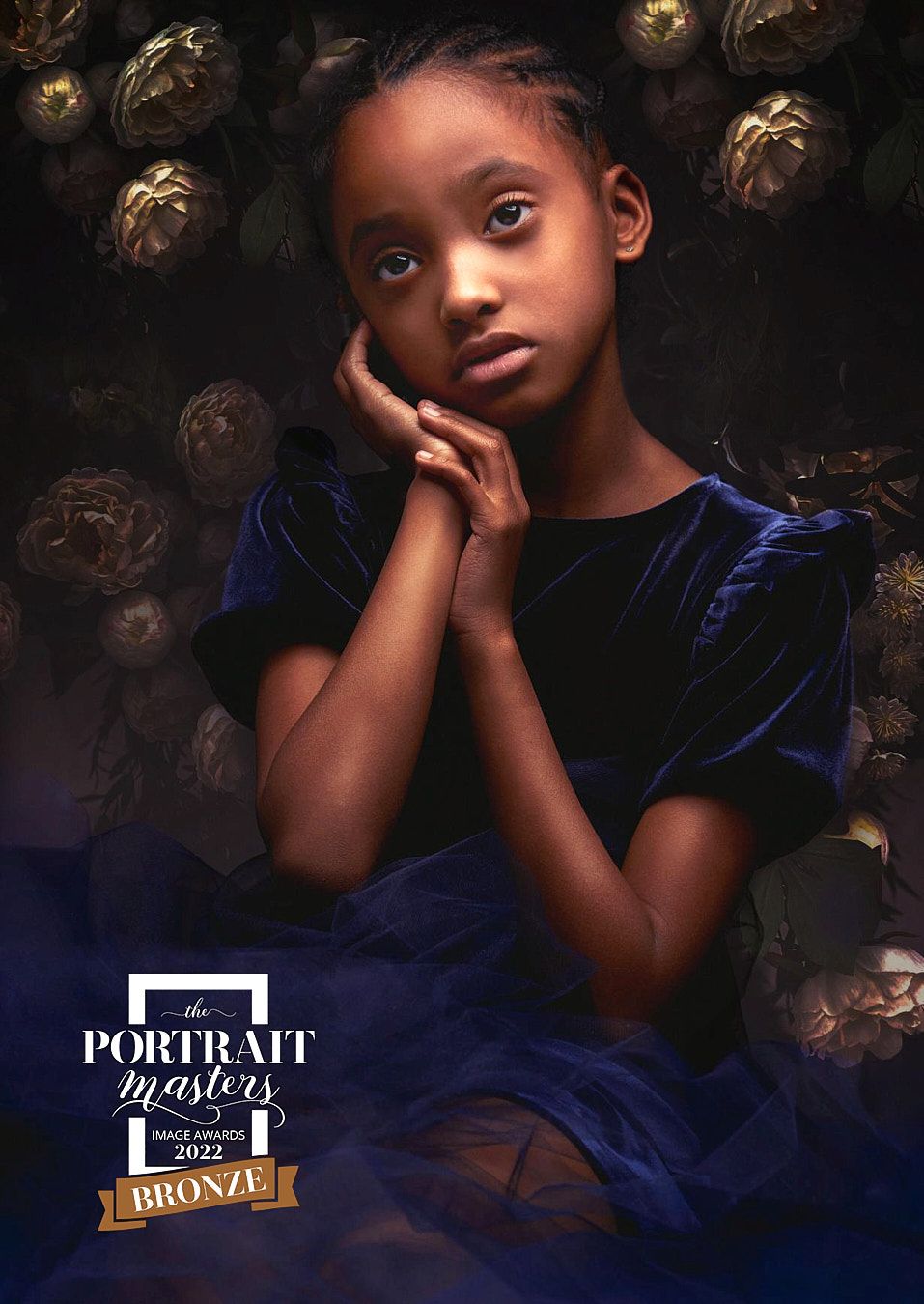 Young girl in blue velvet dress posing with hands clasped, Portrait Masters 2022 Bronze award.