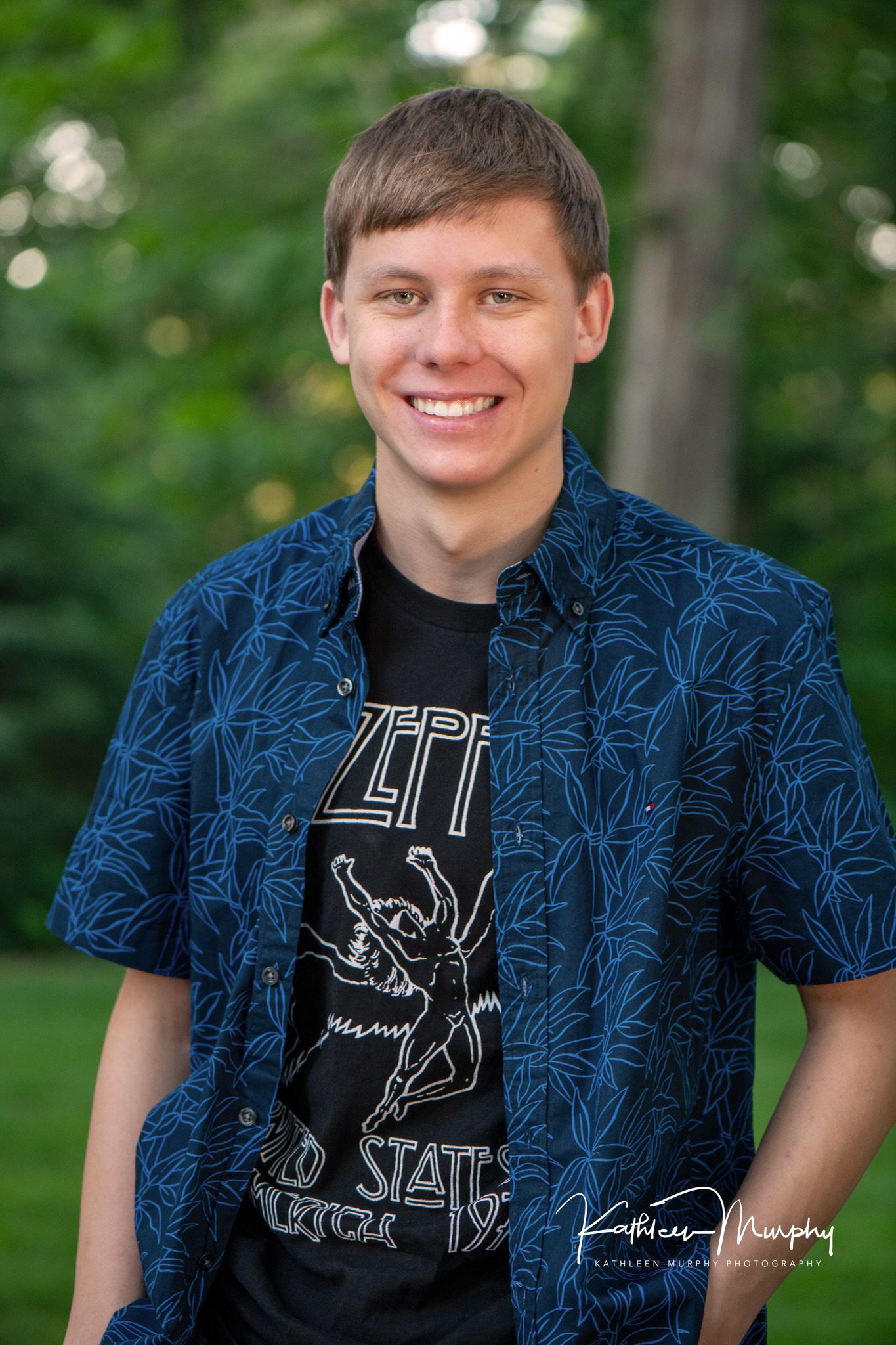Person wearing blue patterned short sleeve shirt with Zeppelin graphic t-shirt in outdoor setting.