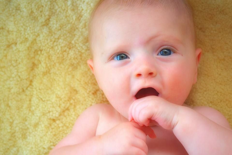 Close-up portrait of an infant with bright blue eyes against a yellow background.