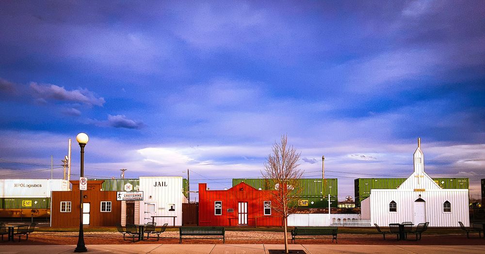 Colorful row of small buildings including a white church under dramatic purple sky.