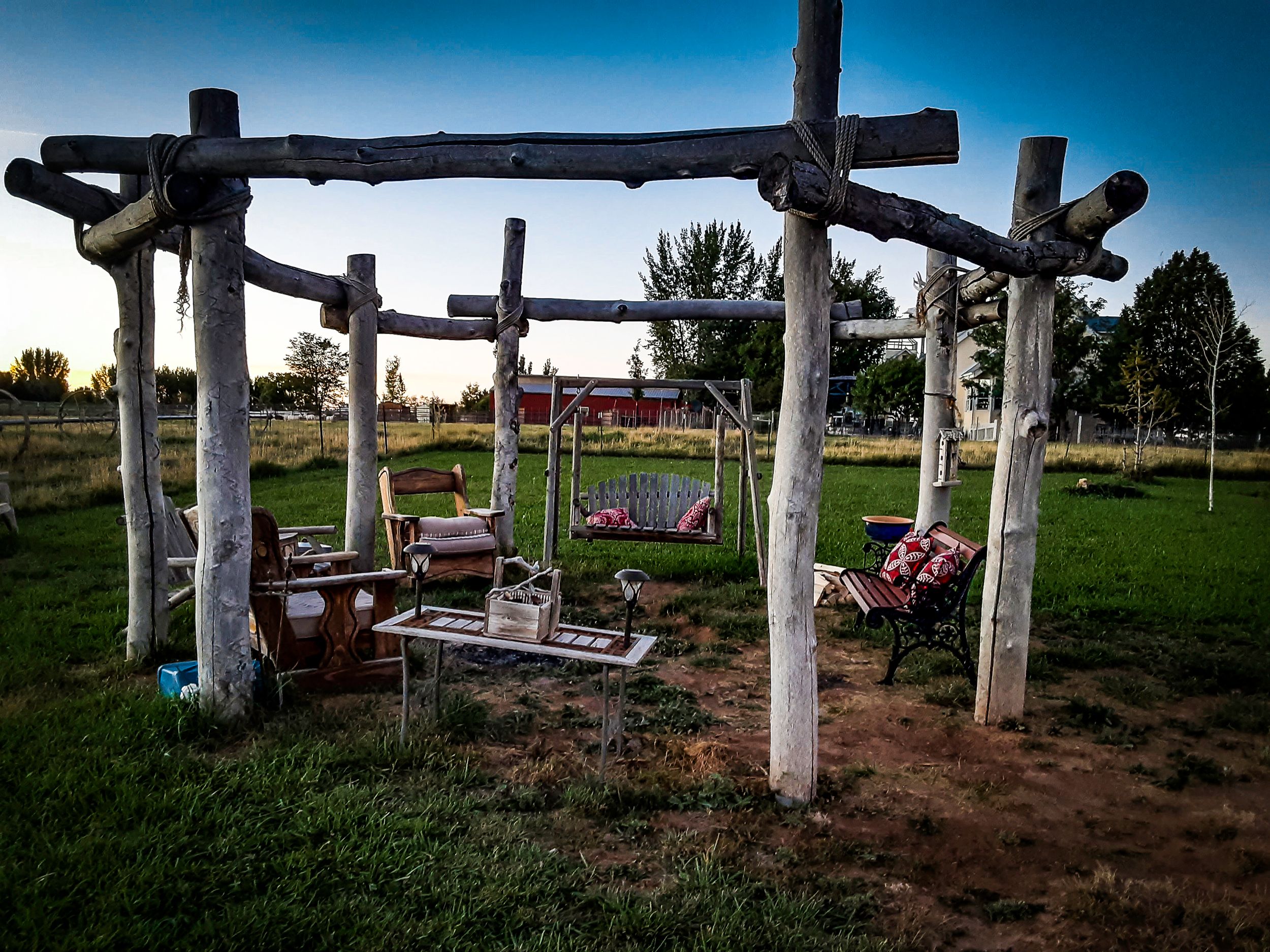 Rustic wooden pergola with bench seating in a peaceful countryside garden setting at dusk.