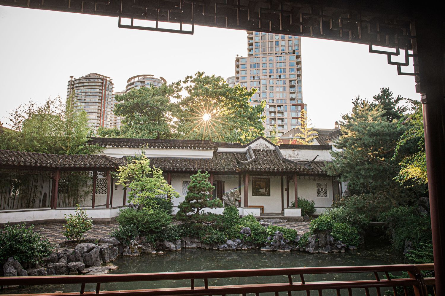 Traditional Chinese garden pavilion with modern high-rise buildings visible in the background through ornate architecture.