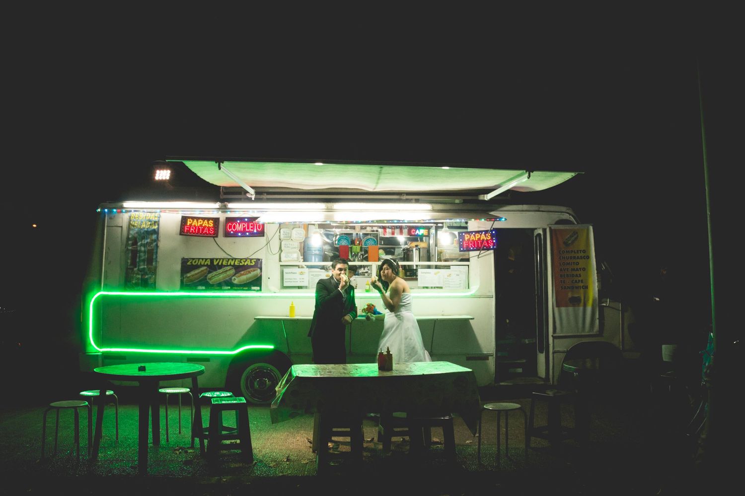 Illuminated food truck at night with green lighting and bar stools creating an atmospheric dining scene.