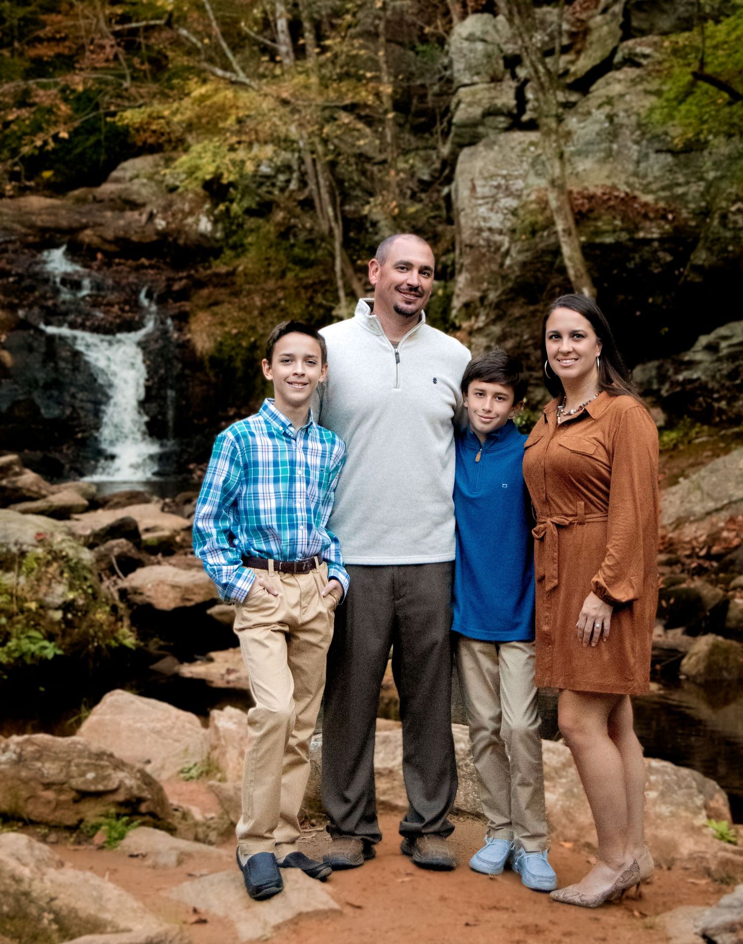 Family poses together on rocky terrain near a scenic waterfall in casual outdoor attire.