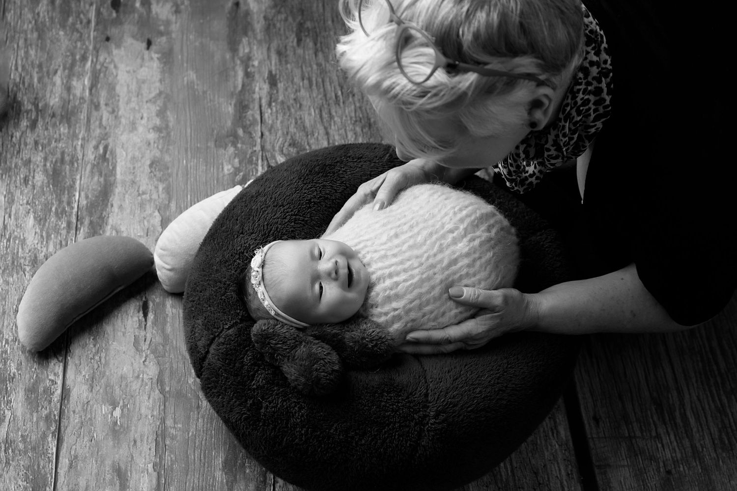 Black and white image of baby resting on round cushion with caregiver nearby.