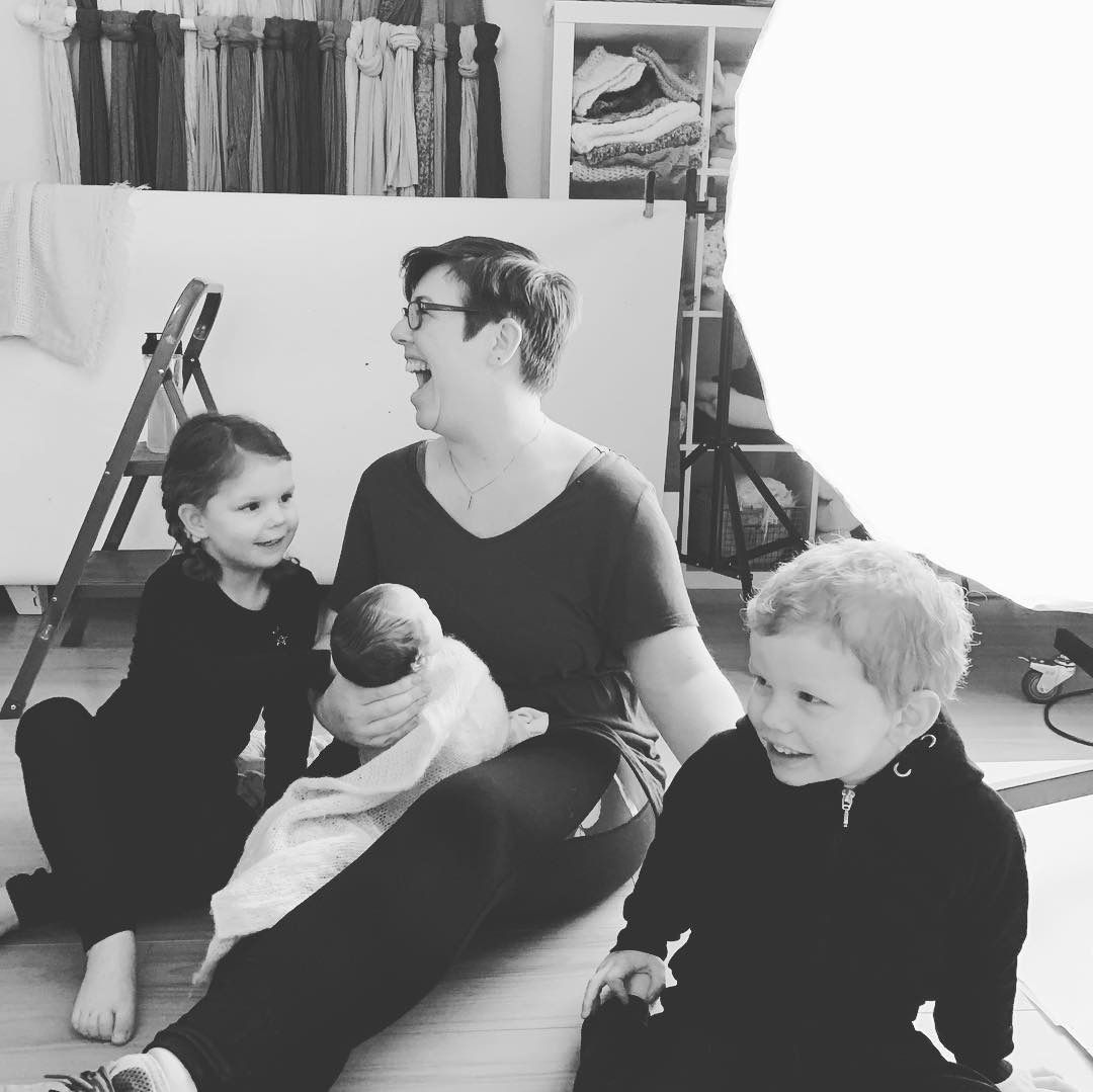Family gathered on floor during indoor photo session with clothing rack in background.