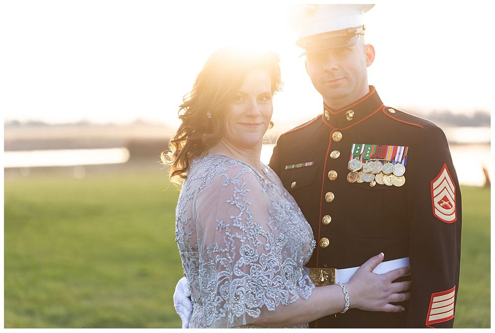 Marine in dress blues holds bride in lace gown during golden hour outdoor wedding portrait.