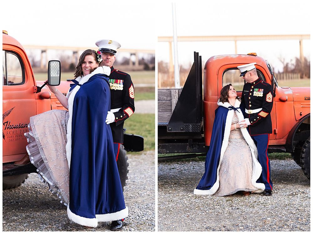 Bride in navy blue cape and Marine groom pose beside vintage orange truck at winter wedding.