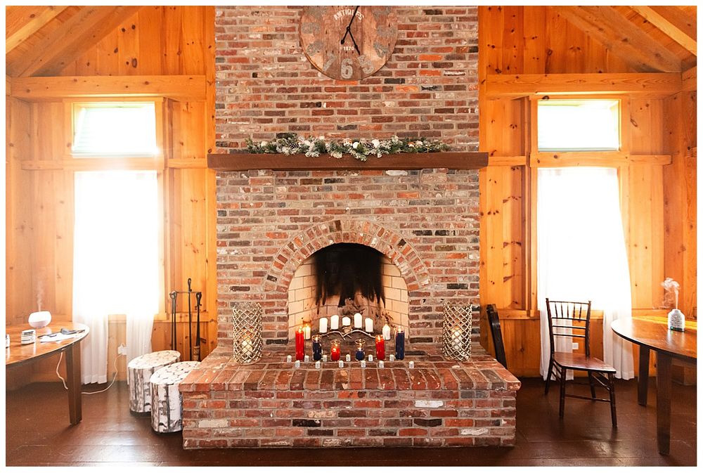 Elegant brick fireplace with candles and greenery garland in rustic wood-paneled wedding venue.