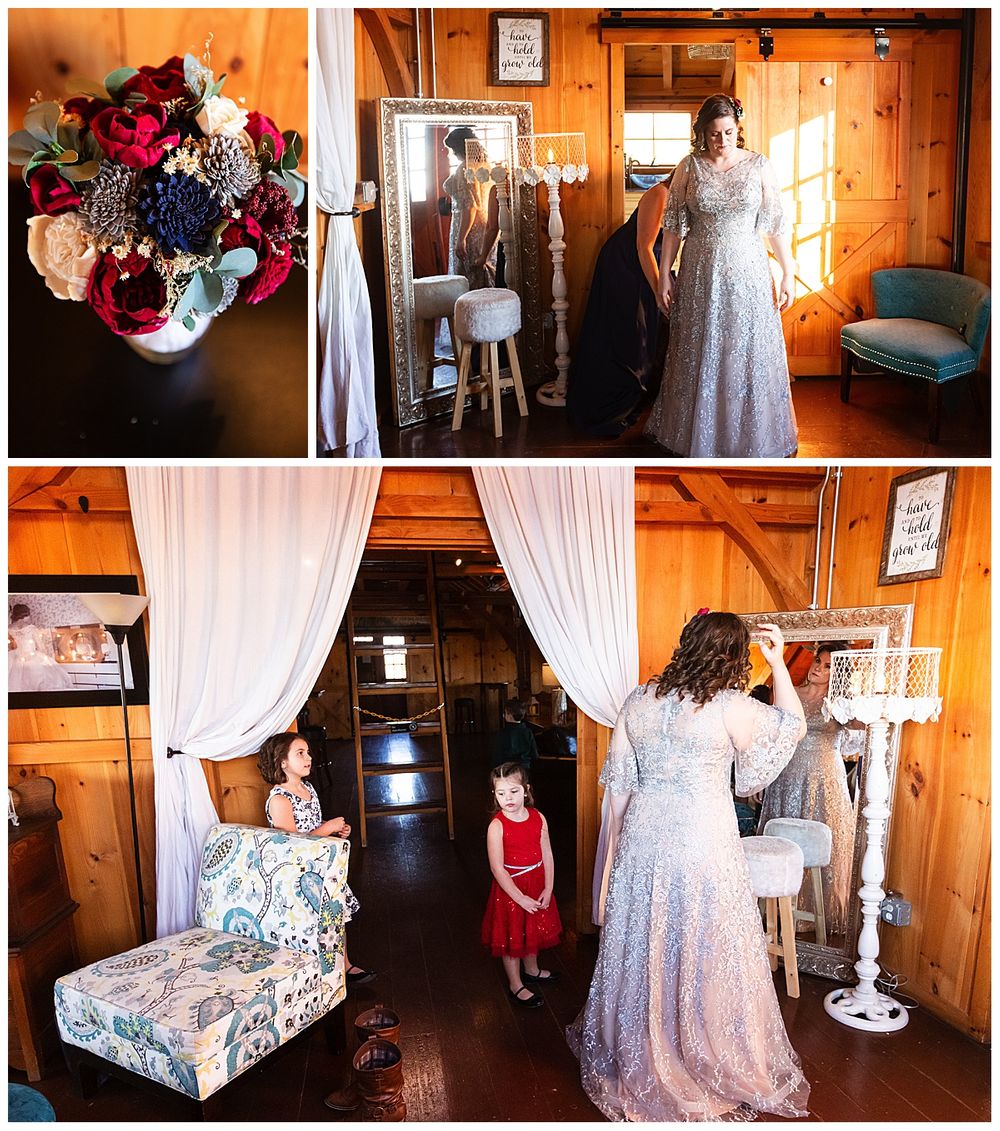 Bride in silver lace dress with colorful bouquet and two girls in red dresses in barn.