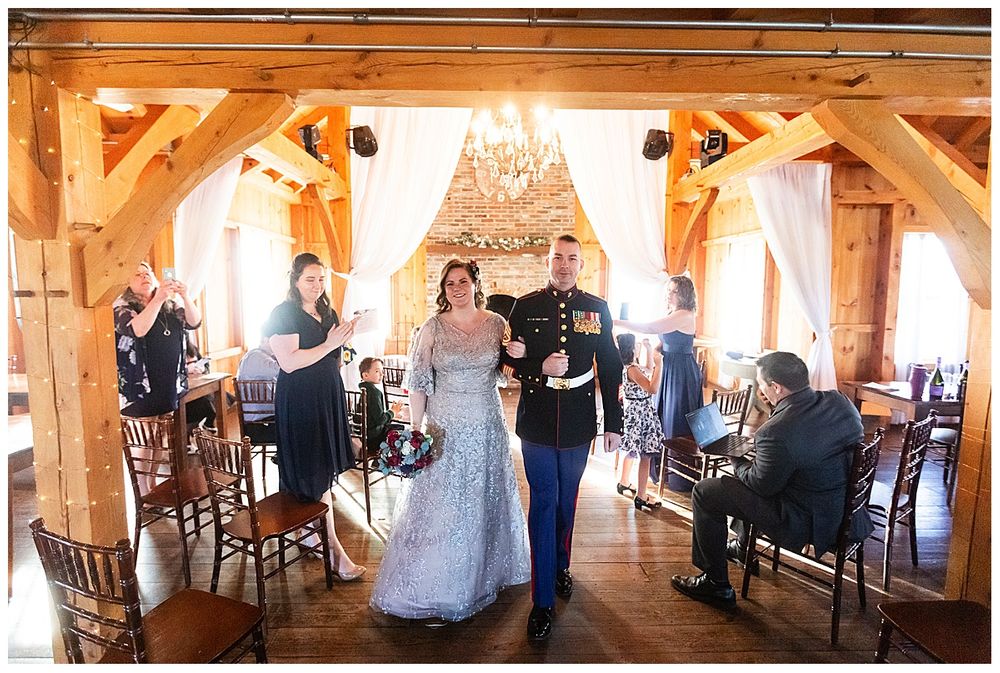 Newlywed couple walks back down aisle as guests applaud in rustic barn wedding reception venue.