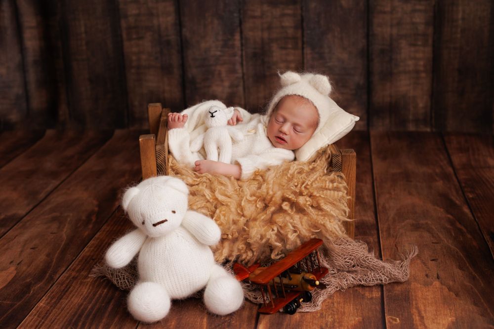 Newborn sleeping in wooden basket with white teddy bear and holiday decorations.