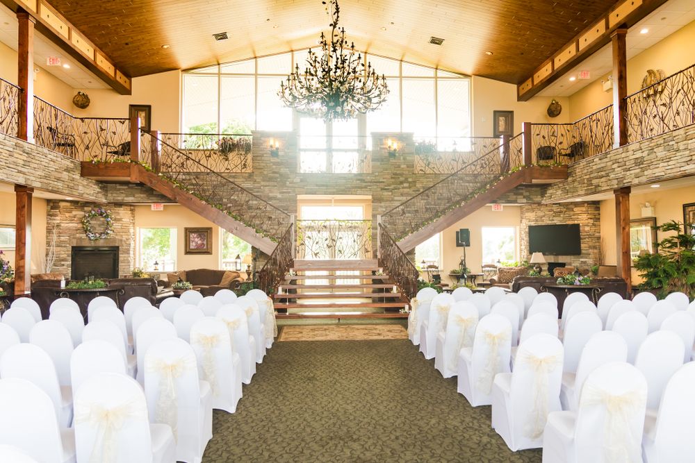 Elegant wedding venue with grand staircase, chandelier and rows of white-covered chairs.
